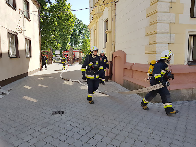 Strażacy rozciągają wąż pożarniczy podczas ćwiczeń w Domu Pomocy Społecznej w Wieleniu.