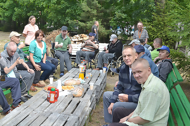 Mieszkańcy DPS w Wieleniu spożywają wspólny posiłek siedząc na ławkach przy stołach z palet.